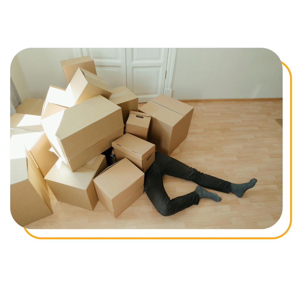 A person is lying under brown cardboard boxes
