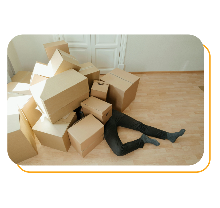 A person is lying under brown cardboard boxes