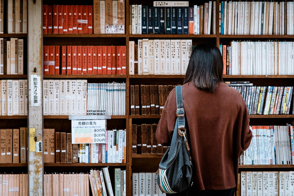 A woman with a brown shirt standing in front of the library books